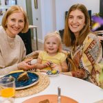 Three generations of smiling women enjoying a meal together indoors.