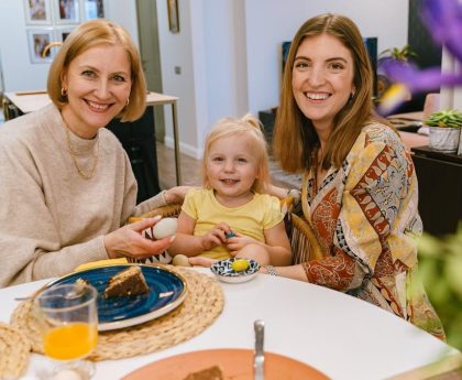Three generations of smiling women enjoying a meal together indoors.