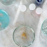 A top-down view of petri dishes and lab equipment on marble with blue liquid and golden particles.