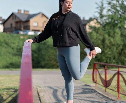 Young woman in activewear stretching on a red railing outdoors.